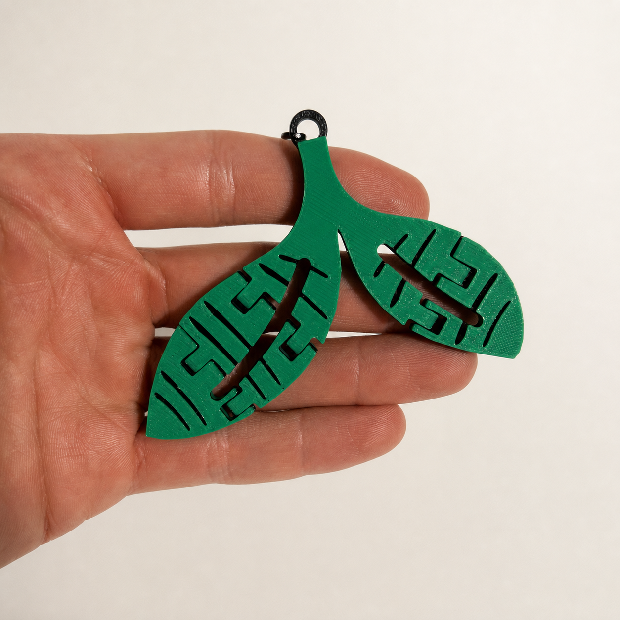 Green-and-black Sprout trinket held in a hand to show scale